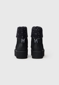 Botas negras hasta el tobillo con un collar texturizado y plegable, diseño minimalista, suela de plataforma de goma y detalles de costura en contraste.