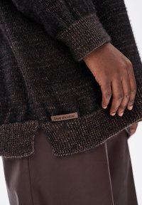 Sweter dzianinowy w ciemnych odcieniach z teksturalnym wzorem. Posiada ściągacze na mankietach oraz metkę z napisem "niebieski cień" na dole.