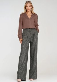 Brązowa bluzka z dekoltem w serek zestawiona z wysokim stanem, szerokimi spodniami z szarego tkanego materiału. Ubranie charakteryzuje się miękką tkaniną i wyraźną sylwetką.