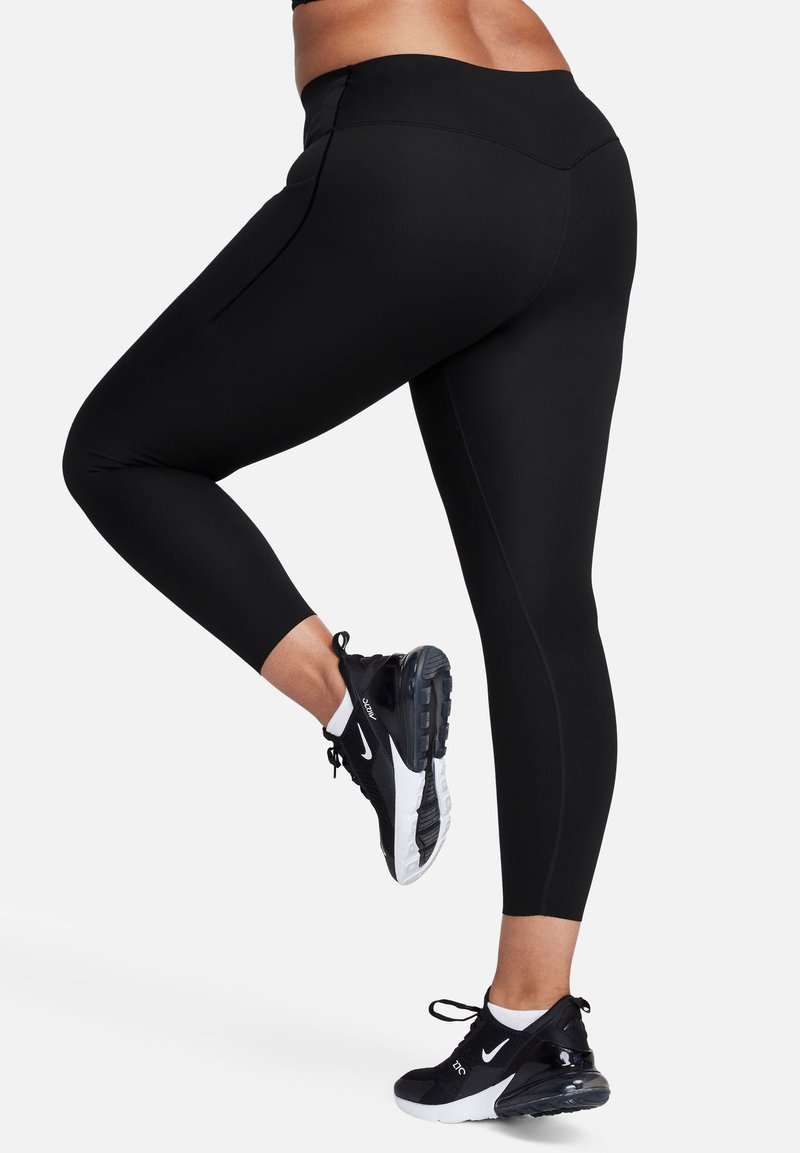 Leggings deportivas negras con cintura alta y costuras laterales, combinadas con zapatillas Nike en blanco y negro con suela acolchada.