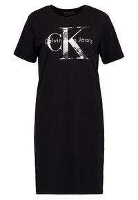 Svart kortärmad T-shirtklänning i bomull med en stor silverlogotyp som säger "Calvin Klein Jeans." Enkel design, avslappnad passform.