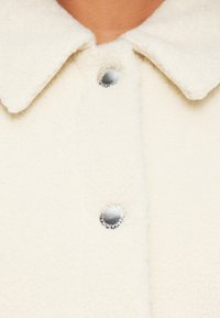 Valge tekstuuriga fliisjakk krae ja trukknappidega. Omab metallseid aktsente ning pehmet ja sooja materjali, sobib jahedamateks ilmadeks.