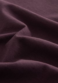 Tessuto viola scuro, trama liscia con lieve lucentezza, presenta pieghe e piegature morbide, mostrando un design elastico e leggero.