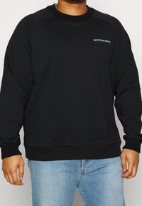 Black sweatshirt with ribbed cuffs and hem, featuring a small blue logo "SCOTCH & SODA" on the chest, made of soft material.