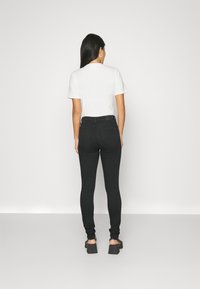 Jeans ajustados de tiro alto negros combinados con una camiseta blanca, mostrando una textura suave y una silueta ceñida desde la vista trasera.