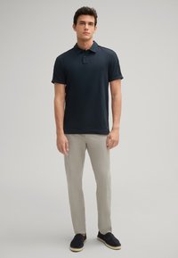 Marineblaues Polo-Shirt mit kurzen Ärmeln und Kragen, kombiniert mit hellgrauen strukturierten Hosen und schwarzen Slippern mit geflochtener Sohle.