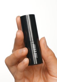 Tube de rouge à lèvres cylindrique noir tenu dans une main, finition brillante avec le texte blanc "LORD & BERRY", texture lisse, taille compacte.