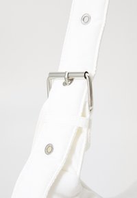 White fabric strap with a silver metal buckle and rivet detail. Smooth texture and clean stitched edges. Close-up of fastening mechanism.