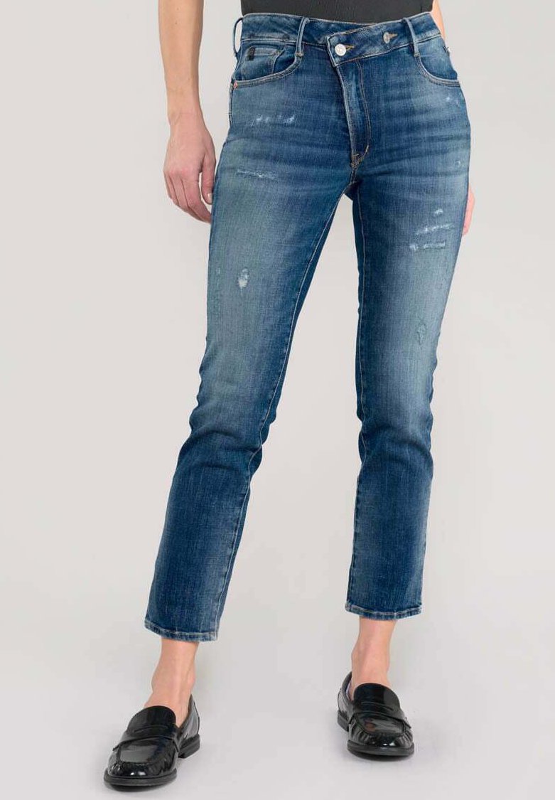 Jean en denim bleu avec un délavage, des détails usés et une coupe droite, associés à des mocassins noirs brillants.