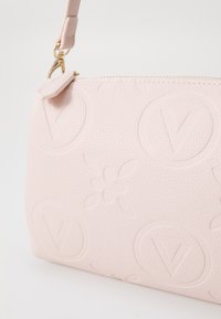 Sac à main en cuir rose clair avec logos V en relief et motif floral. Il dispose d'une fermeture éclair et d'une bandoulière détachable. Texture lisse.