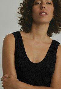 Top a righe nera con scollatura a barchetta e spalline larghe, che mette in mostra un tessuto testurizzato e una silhouette aderente.