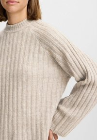 Suéter de punto acanalado beige con un cuello alto y mangas raglán. La textura es suave, de peso pesado y tiene un ajuste holgado.