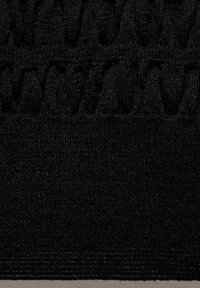 Tissu tricoté noir présentant des motifs texturés complexes, avec une section inférieure lisse et des détails bouclets en relief près du sommet.