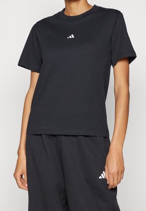 Osoba nosząca czarną koszulkę z krótkim rękawem Adidas oraz pasujące czarne spodenki, oba z małymi białymi logo Adidas.