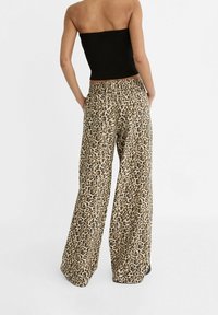 Pantalon large imprimé léopard avec un tissu doux, une ceinture élastique, et une coupe ample. Fond beige avec des taches marron foncé.