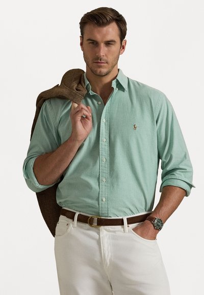 Minta zaļa pogu krekls ar garām piedurknēm, valkāts ar baltām biksēm un brūnu jostu. Tekstūra brūna jakas uzsviesta pār vienu plecu.