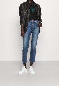 Černá kožená košile, grafické tričko s tyrkysovým vzorem, světle modré džínsy s vysokým pasem, zkrácená délka, bílé tenisky s černými akcenty.