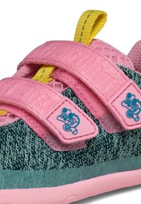 Kindersneaker mit grünem Strickgewebe, pinkfarbenen verstellbaren Riemen mit blauem Froschlogo und gelbem Zuglasche auf weißem Hintergrund.