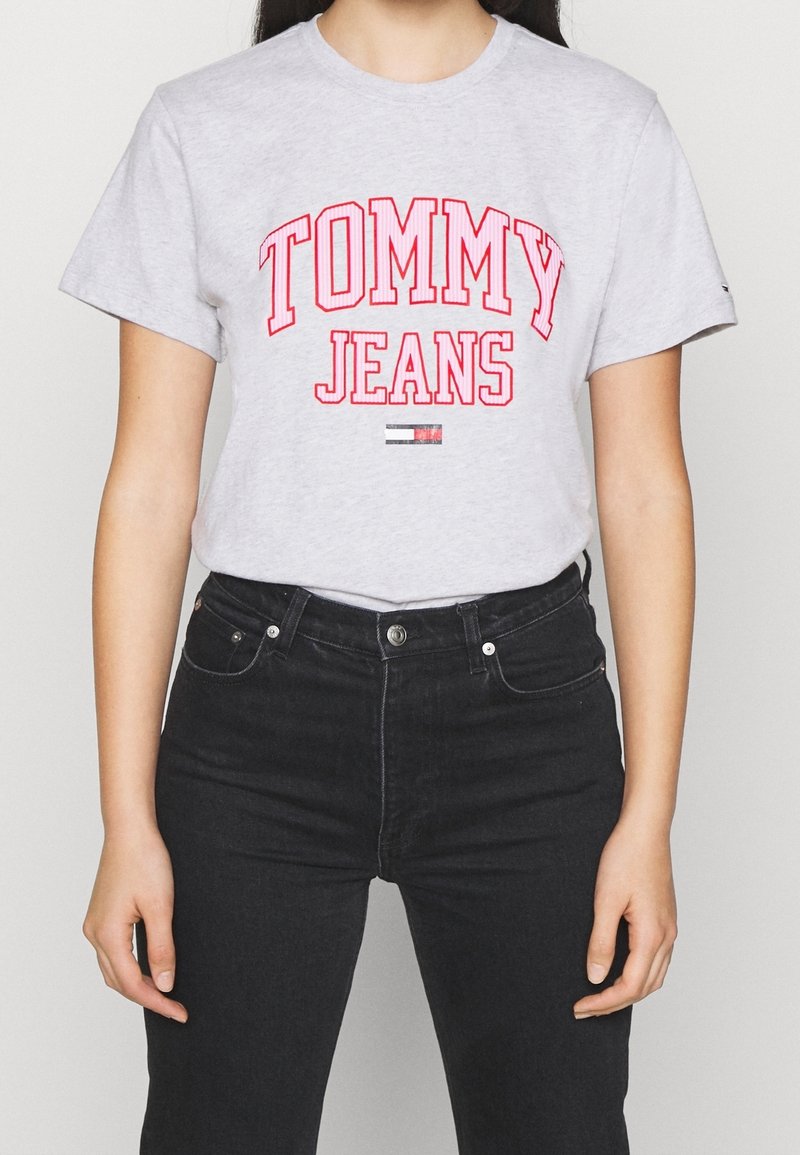 Šedé bavlněné tričko s nápisem "TOMMY JEANS" vytištěným tučnými červenými písmeny. V kombinaci s černými džíny s klasickým střihem.