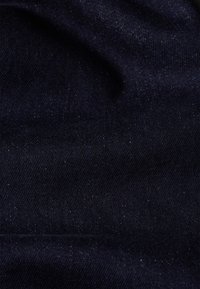 Dark denim fabric displaying a smooth texture with subtle, varying shades of blue and small specks of lighter blue throughout.