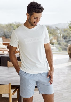 Hvid kortærmet t-shirt med en subtil "JBS OF DENMARK" print, parret med blå og hvide stribede shorts. Casual pasform, glat tekstur.