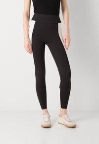 Leggings neri con pannelli laterali crema, vita alta e tessuto elasticizzato. Abbinate a sneakers chiare con lacci e suola in gomma.