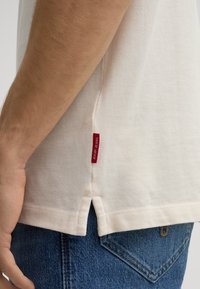 Lichtbeige katoenen t-shirt met zijsplitten en een rode "Joopi Jeans" label. Draag het over donkerblauwe denim jeans met een klassiek zakontwerp.