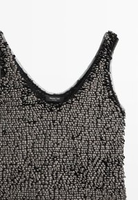 Zwart getextureerd tanktop met verhoogde, afgeronde versieringen, een ronde halslijn en een licht doorzichtige stof.