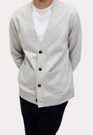 Hellgrauer Cardigan aus weichem Stoff, mit V-Ausschnitt, durchgeknöpft und zwei frontalen Taschen. Mit dunkelbraunen Knöpfen akzentuiert.