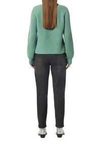 Mintgrüner gerippter Pullover mit Raglanärmeln, kombiniert mit schmal geschnittenen dunkelgrauen Jeans und silbernen Stiefeletten, von hinten betrachtet.