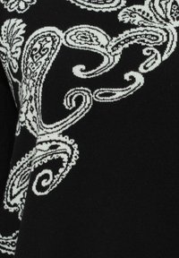 Tissu noir avec des motifs tricotés en forme de paisley et floraux blancs formant des dessins tourbillonnants et complexes.