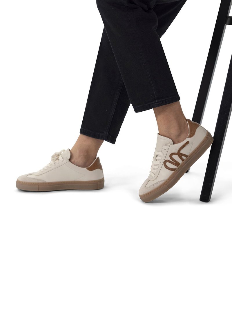 Beige sneakers with brown accents, smooth leather upper, rounded toe, flat rubber sole, and contrasting stitching detail.