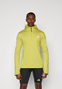 Hellgrüner Pullover mit Reißverschluss am Hals und Kapuze. Besitzt weiße Adidas-Logos auf der Brust und den Ärmeln. Glatte Textur, sportliche Passform.