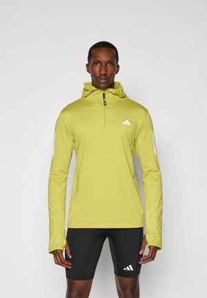 Hellgrüner Pullover mit Reißverschluss am Hals und Kapuze. Besitzt weiße Adidas-Logos auf der Brust und den Ärmeln. Glatte Textur, sportliche Passform.