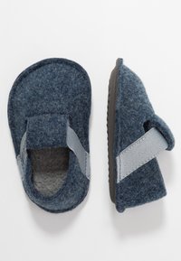Chaussons doux pour tout-petits en bleu avec des bandes élastiques grises et des semelles texturées, présentés de dessus et de côté sur un fond blanc.