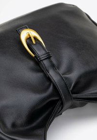 Bolso de mano de cuero negro con una superficie texturizada, que presenta un prominente detalle de hebilla dorada y un diseño suave y recogido.