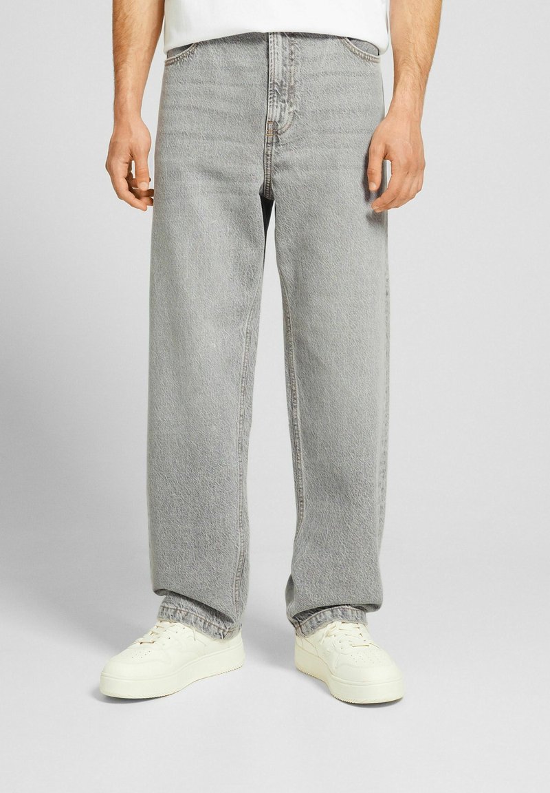Jeans en denim gris clair avec une coupe décontractée, présentant une texture légèrement décolorée, des coutures typiques et un design taille haute.