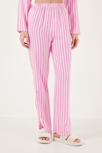 Person in rosa-weiß gestreiften, vertikalen Schlafanzughosen und weißen, flauschigen, offenen Hausschuhen, stehend vor einem schlichten hellen Hintergrund.