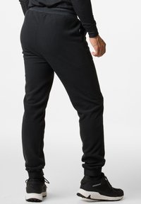 Zwarte fleece joggers met elastische boorden en tailleband, voorzien van zijzakken en een klein logo-detail bij de taille. Gecombineerd met zwarte sneakers.