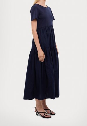 Tmavě modré bavlněné midi šaty s vodorovnými volány, krátkými rukávy a kulatým výstřihem. Doplněné černými páskovými sandály na podpatku.
