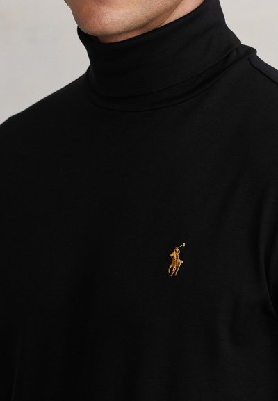 Mees kannab musta kõrge kaelusega kampsunit, millel on rinnal väike kuldse tikandiga polo mängija logo.