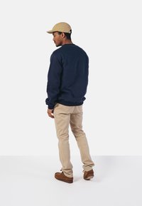 Sudadera de marina, gorra caqui, pantalones beige claros, zapatos marrones. Enfocado en un ajuste relajado, textura suave y diseño simple sin logotipos visibles.