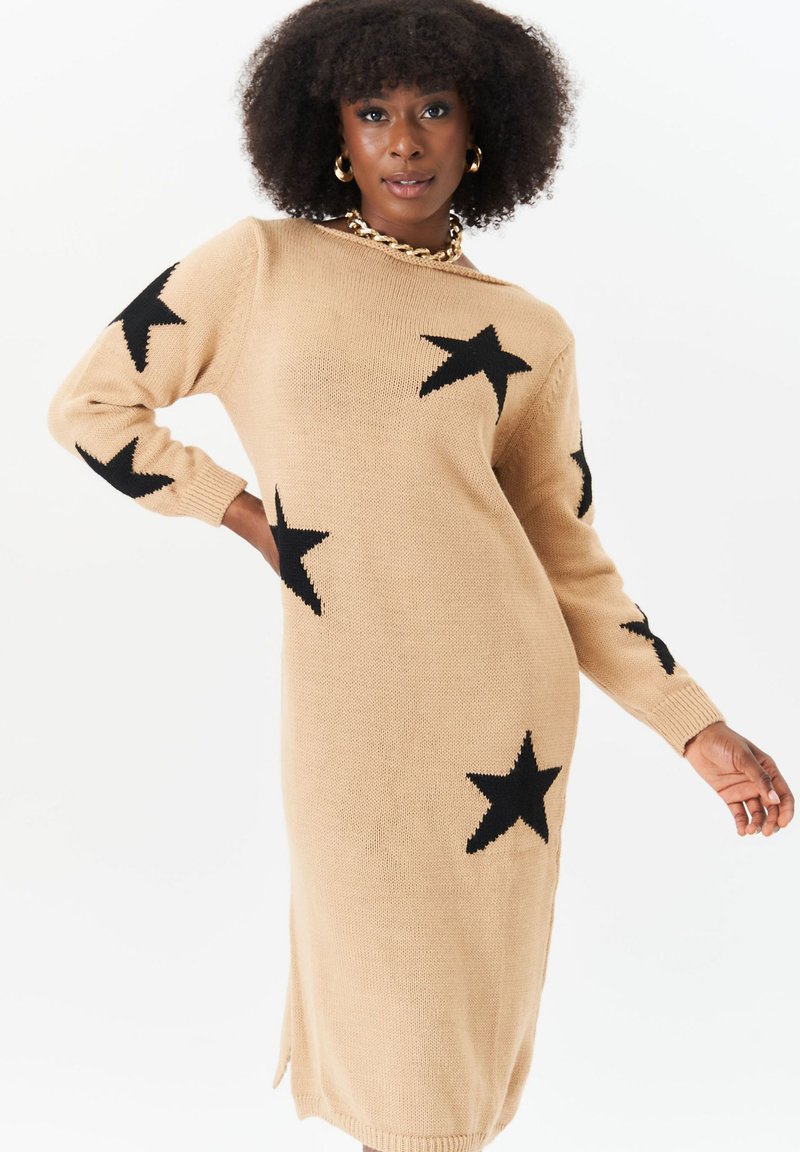 Beige knitted dress featuring large black star patterns, long sleeves, ribbed cuffs, and side slits for ease of movement.