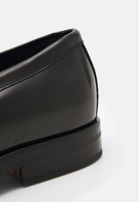 Talons de chaussures habillées en cuir noir poli avec coutures visibles et logo embossé "BOSS" sur le côté supérieur.