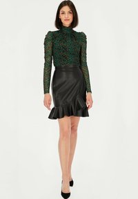 Zielona i czarna bluzka w lamparta z długim rękawem i wysokim kołnierzem, połączona z dopasowaną czarną skórzaną spódnicą z falbanami.