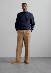 Navy blue sweatshirt with crew neckline and small logo, paired with beige trousers and tan sneakers. Smooth fabric and relaxed fit.