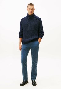 Maglione a collo alto a coste in maglia colore navy con una vestibilità comoda, abbinato a pantaloni taper a blu chiaro e scarpe in pelle nere. Texture liscia.