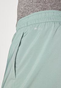 Světlé zelené sportovní šortky vyrobené z hladkého, lehkého materiálu. Obsahují elastický pás a boční kapsy. Viditelné logo DRYCELL.