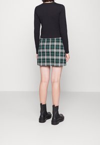 Schwarzes Langarmoberteil kombiniert mit einem grün-weißen karierten Minirock. Getragen mit schwarzen Ankle-Boots. Glatte Textur, figurbetontes Design.