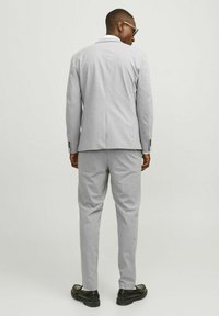 Light grey suit made of soft fabric. The jacket has a notch lapel and the pants are tailored. Simple black shoes complete the outfit.